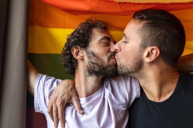 Gepassioneerd homopaar zoent met lgbtq-vlag op de achtergrond Jong homopaar hecht liefdevol binnenshuis