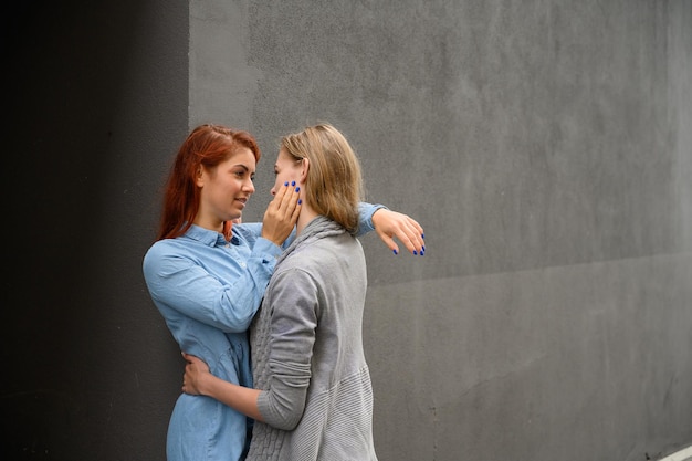 Gepassioneerd liefdevol lesbisch stel Twee mooie jonge vrouwen knuffelen teder buitenshuis tegen een grijze muur LGBT-commune Meisjes op een date