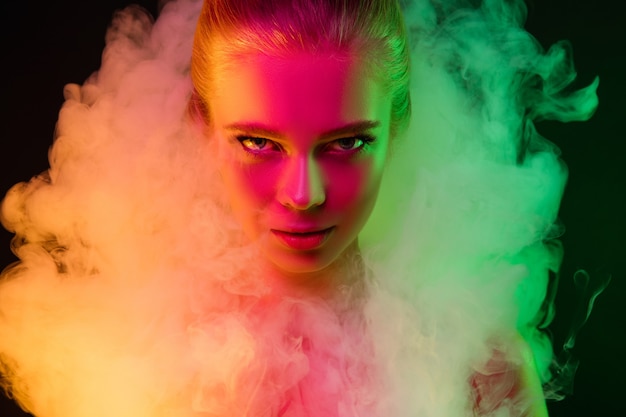 Gepassioneerd. Portret van vrouwelijke mannequin in neonlicht op donkere studioachtergrond met rook. Mooie blanke vrouw met trendy make-up en verzorgde huid. Levendige stijl, schoonheidsconcept. Detailopname.