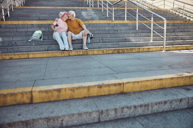 Gepassioneerde grijsharige vrouw met een bidon in haar hand die haar tevreden oudere echtgenoot kust