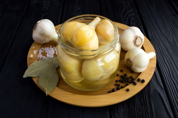 Gepekelde knoflook in de glazen pot op de bruine snijplank op de zwarte houten