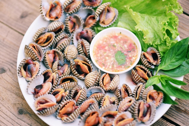 Gepelde kokkels met zeevruchtensaus en groentesaladesla op plaat houten achtergrond Verse rauwe schelpdieren bloed kokkel oceaan gastronomische zeevruchten in het restaurant zeeschelpen eten