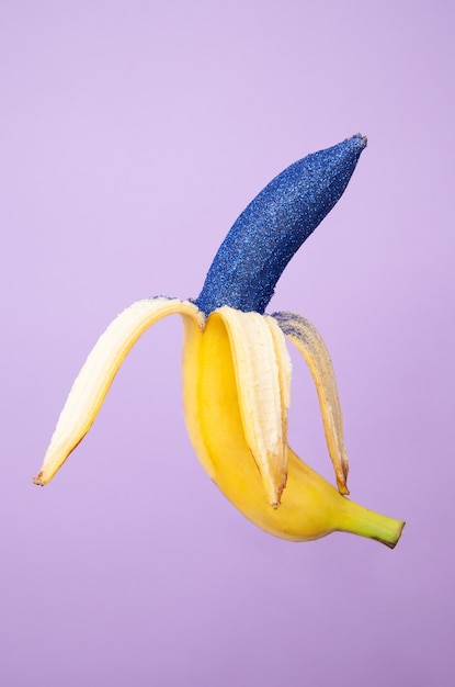 Gepelde rijpe banaan bedekt met glinsterende verf van heldere blauwe kleur en geïsoleerd op paarse achtergrond