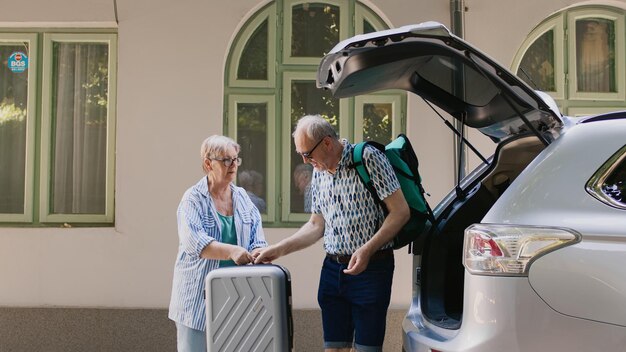 Gepensioneerd echtpaar dat reisbagage in de kofferbak laadt terwijl ze op huwelijksverjaardag zomer stedentrip gaan. oudere toeristen maken zich klaar voor een excursie terwijl ze bagage en trolleys in het voertuig plaatsen