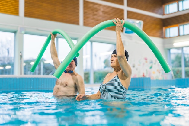 Gepensioneerd echtpaar met zwemnoedels en aerobics in het zwembad actief senior leven