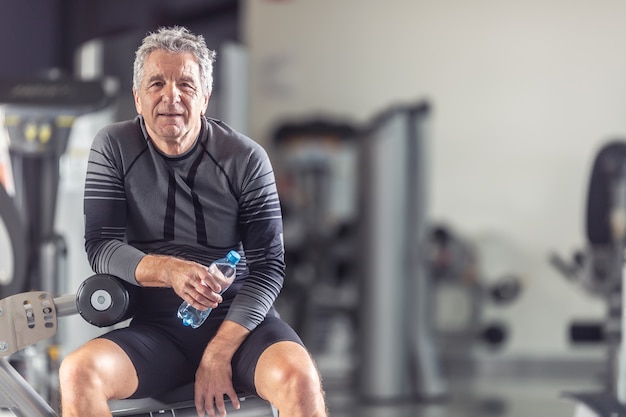 Gepensioneerde houdt zichzelf fit door te sporten in een sportschool, uit te rusten met een fles water.