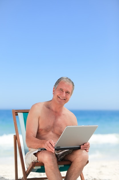 Gepensioneerde man aan het werk op zijn laptop op het strand