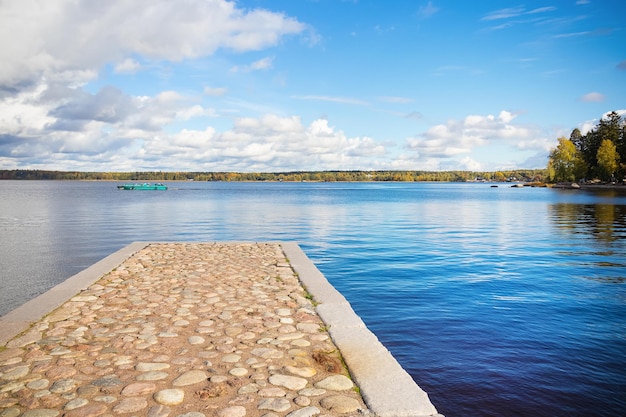 Foto geplaveide pier en blauw meer water blauwe lucht en witte wolken bomen aan de horizon en boot