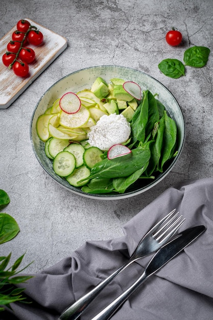 Gepocheerd ei. Groene salade met avocado, komkommer, spinaziebladeren, courgette en radijs in een bord op een grijze stenen tafel. Restaurant menu