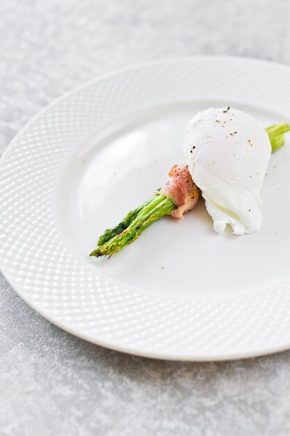 Gepocheerd ei op geroosterde asperges gewikkeld in spek.