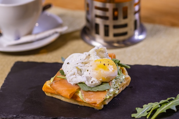 Gepocheerd ei op toast, met gerookte zalm, avocado, gegrilde tomaat en babyspinazie.