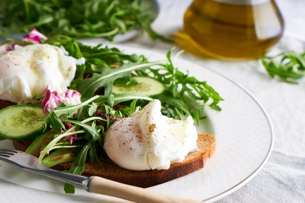 Gepocheerde eieren met kruiden, avocado en komkommer geserveerd op een bord op een lichte achtergrond