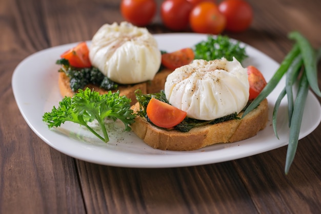 Gepocheerde eieren met sneetjes brood en een bosje groene uien op een witte plaat. Vegetarische snack met gepocheerde eieren.