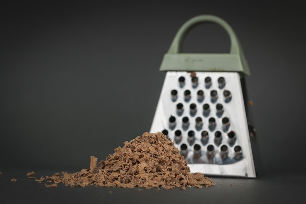 Geraspte chocolade en een metalen rasp op een donkere achtergrond