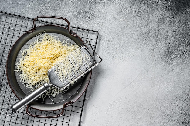 Geraspte kaas voor het koken in een stalen bak met rasp witte achtergrond bovenaanzicht kopie ruimte