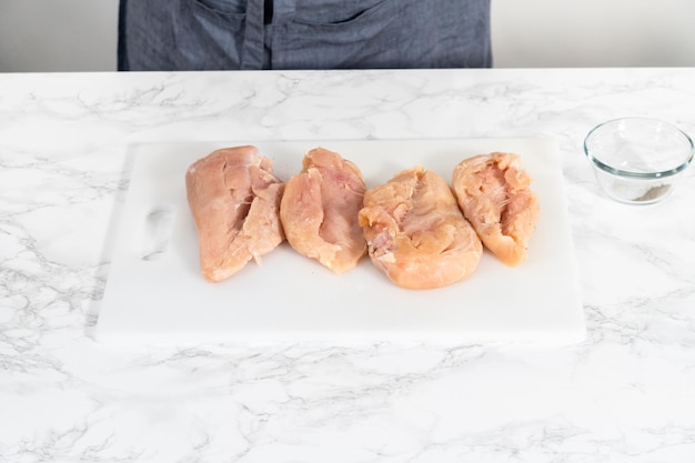 Geraspte kip in een snelkookpan Kipfilet kruiden met zout en gemalen peper op een witte snijplank