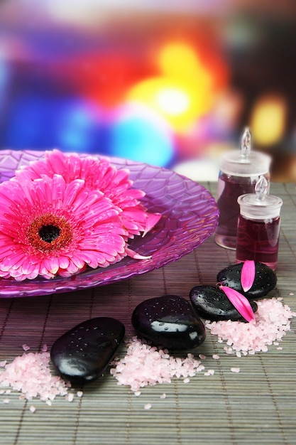 Gerbera flowers on water and spa stones on bamboo mat