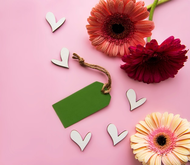 Gerbera  flowers, wooden hearts and green paper tag on a pink pastel. Top view