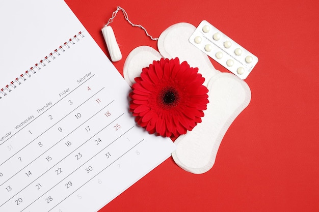 Foto gerbera, menstruatiekalender, pillen en tampons op een rode achtergrond. ovulatie concept. menstruatie concept.