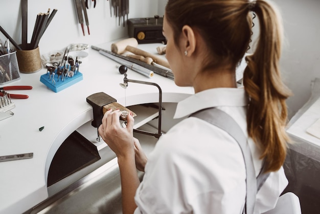 Gericht op werk zijaanzicht van jonge vrouwelijke juwelier die een ring maakt op haar werkbank