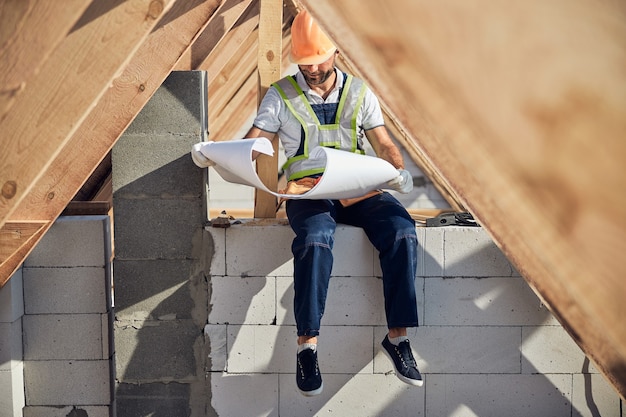 Gerichte architect die een blauwdruk controleert terwijl hij onder een houten dakkarkas zit