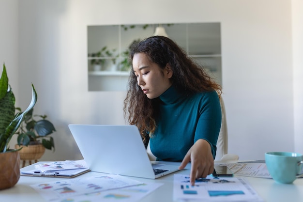 Gerichte aziatische vrouw die laptop thuis gebruikt, naar het scherm kijkt, chat, e-mail leest of schrijft, zittend op de bank, vrouwelijke student die huiswerk maakt, online aan een onderzoeksproject werkt