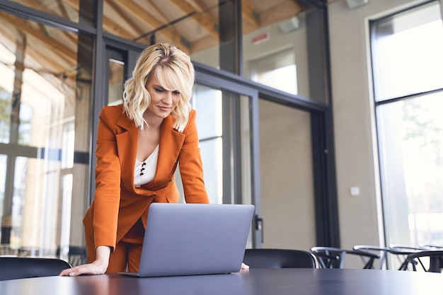 Gerichte blonde jonge vrouwelijke ondernemer die voor een computer staat die op het bureau is geplaatst