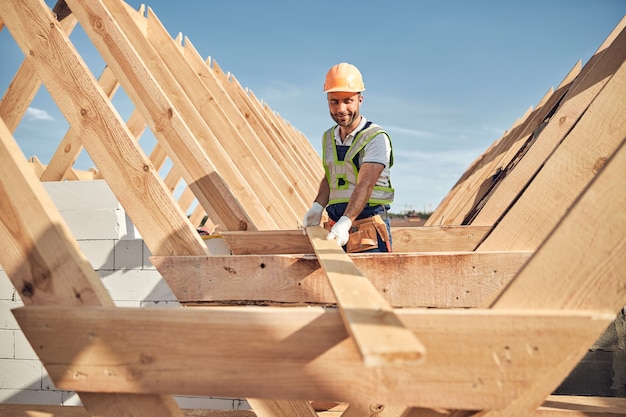 Gerichte bouwer die een veiligheidshelm draagt en een lang stuk hout vasthoudt voor het bouwen van een dakkarkas