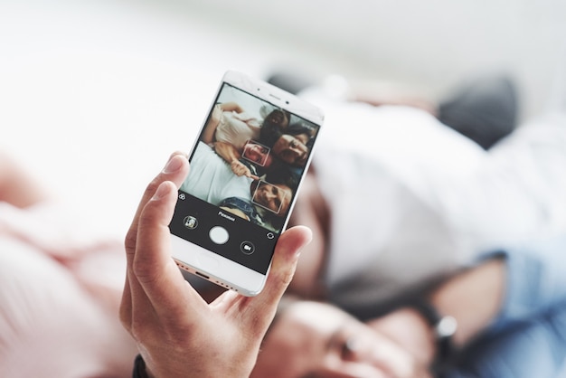 Gerichte foto van de telefoon die wordt vastgehouden door een man die een selfie neemt met vrienden die gaan liggen