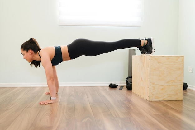 Gerichte gelukkige vrouw die thuis een uitdagende trainingsroutine doet met een springdoos. Blanke vrouw doet push-ups en crosstraining