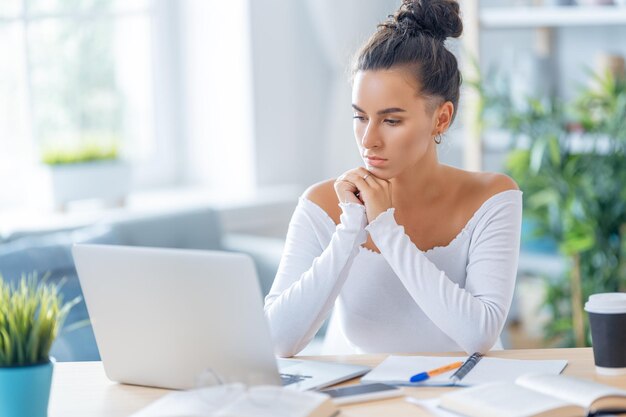 Gerichte jonge zakenvrouw die online studeert, webinar, podcast op laptop kijkt, aantekeningen maakt, aan het bureau zit. E-learningconcept.