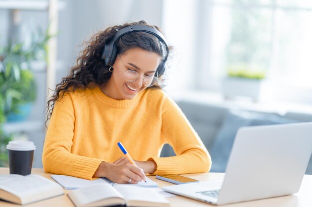 Gerichte jonge zakenvrouw die online studeert, webinar, podcast op laptop kijkt, aantekeningen maakt, aan het bureau zit. E-learningconcept.