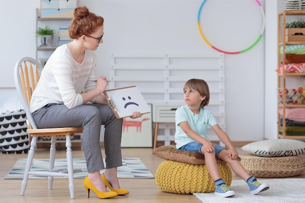 Foto gerichte jongen zittend op een gele poef in gesprek met een counselor zittend op een stoel in de klas