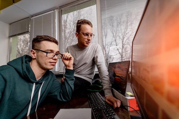 Gerichte jongensstudenten met een bril die op het scherm van de computer kijken. Teamwerk in moderne werkplek.