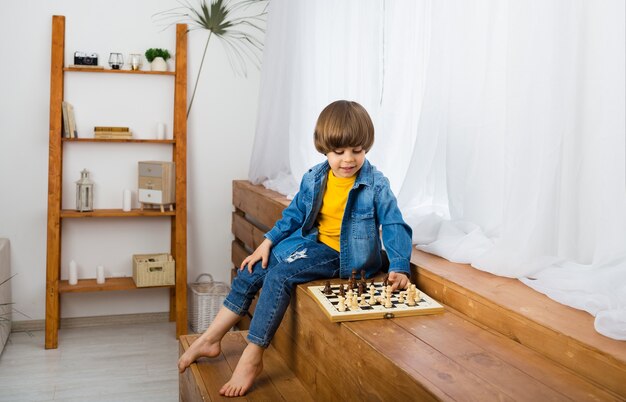Gerichte kleine jongen zit in een kamer en speelt schaak
