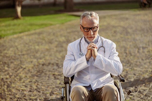 Gerichte senior gehandicapte mannelijke arts in rolstoel met laboratoriumjas en bril die een pauze neemt