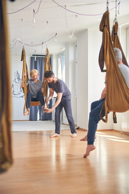 Gerichte serieuze donkerharige gecertificeerde jonge blanke luchtyoga-instructeur die de regelaar op de hangmat schuift