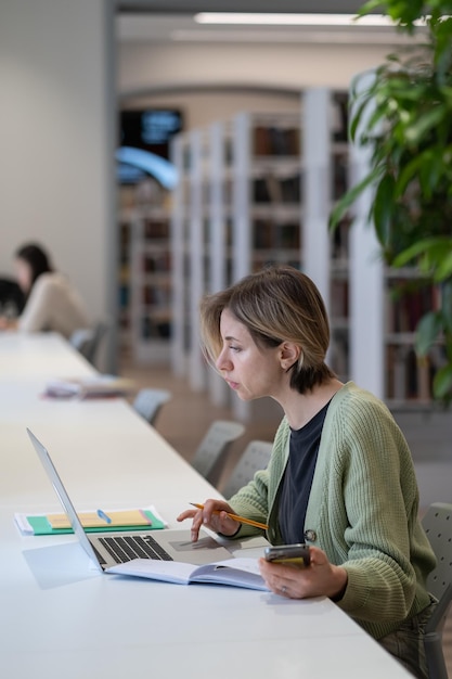 Gerichte vrouwelijke universitair docent die laptop gebruikt terwijl ze in een rustige, gezellige bibliotheek zit