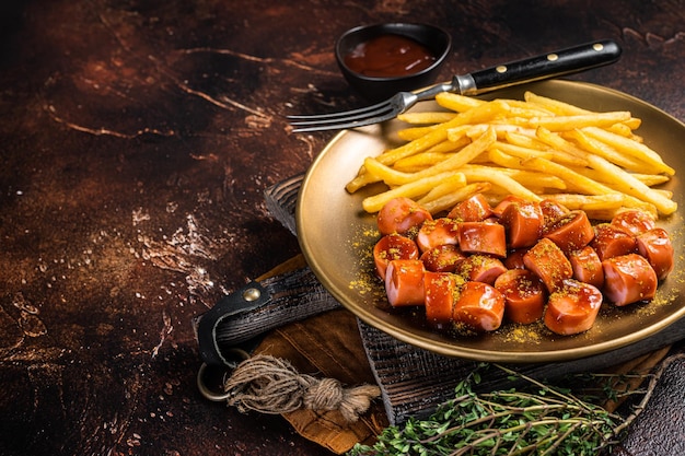 Wurst di salsiccia al curry tedesco servito con patatine fritte sfondo scuro vista dall'alto spazio di copia