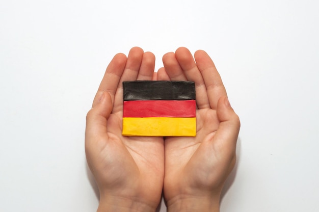 German flag made of plasticine in the hands of a child on a white background