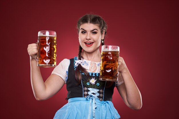 German girl in traditional costume with two large pints of pale\
ale over red background