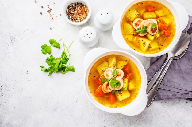 German potato soup with sausages and vegetables in white bowls, white background. 