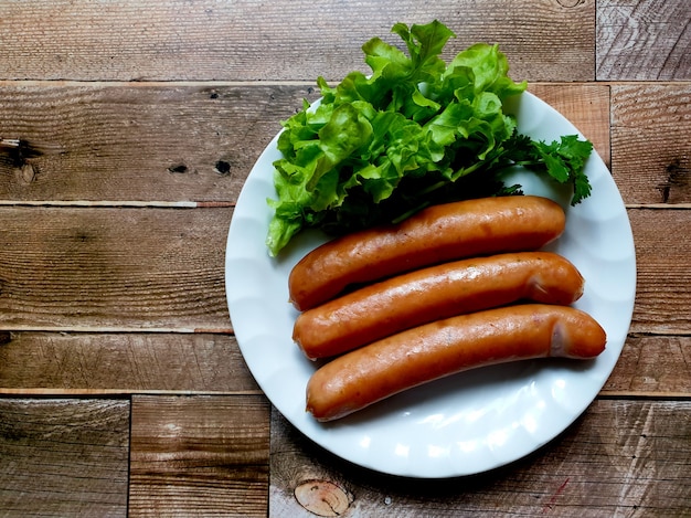 German sausages with green lettuce in a white dish on wooden background