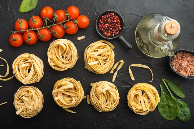 Gerold tagliatelle vorm van italiaanse pasta met ingrediënten set, op zwarte stenen achtergrond, bovenaanzicht plat lag