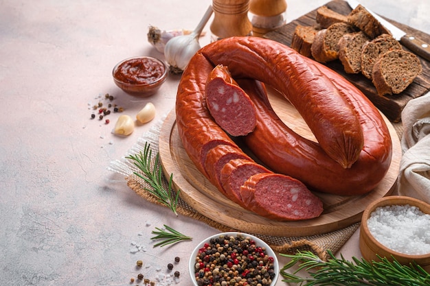 Gerookte, Krakov-worst op een snijplank met brood, knoflook en kruiden op een lichte achtergrond. Zijaanzicht, kopieer ruimte.