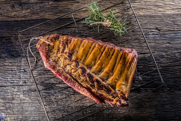 Gerookte rauwe varkensribbetjes en rozemarijnkruiden op een houten bord.