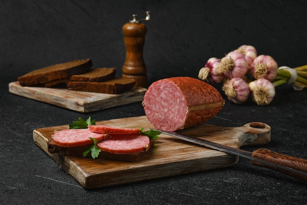 Gerookte salami en sandwich op snijplank op zwarte achtergrond