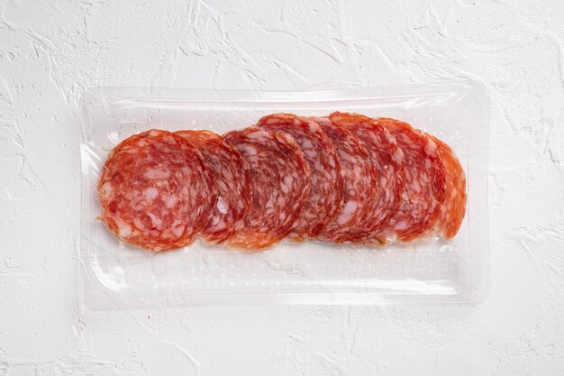 Gerookte salami-worstjes in vacuümverpakking, op witte stenen tafelachtergrond, bovenaanzicht plat gelegd, met kopieerruimte voor tekst