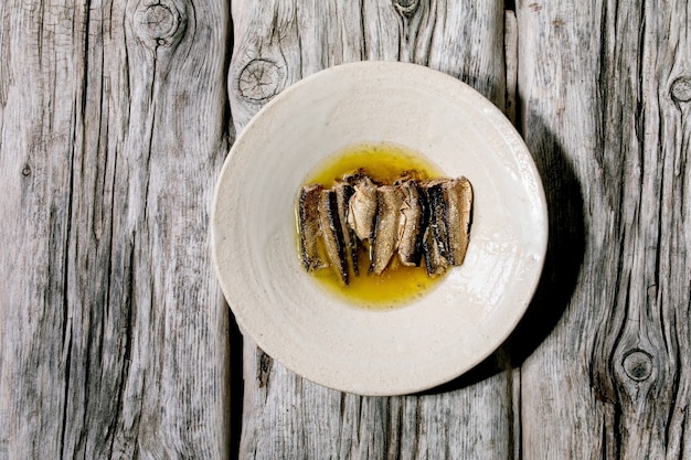 Gerookte sardines in olie geserveerd in witte keramische plaat over oud grijs houten oppervlak. Bovenaanzicht, plat gelegd. Ruimte kopiëren