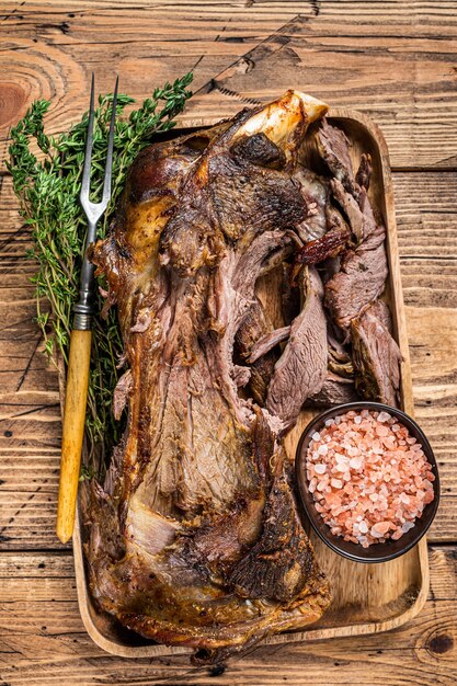 Geroosterd lamsschapenvlees dat schoudervlees in een houten dienblad met vleesvork snijdt